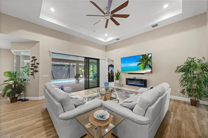 Living room with a raised ceiling, light wood-type flooring, a ceiling fan, and recessed lighting