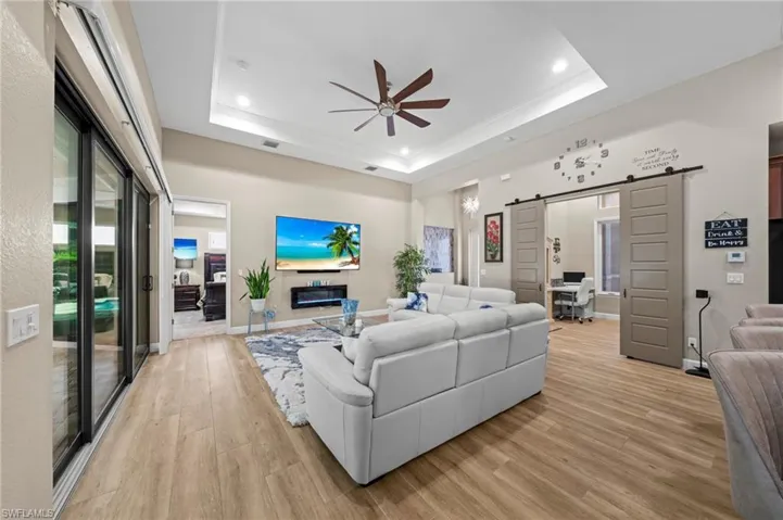 Living room featuring a raised ceiling, light wood-type flooring, a ceiling fan, recessed lighting, and ornamental molding