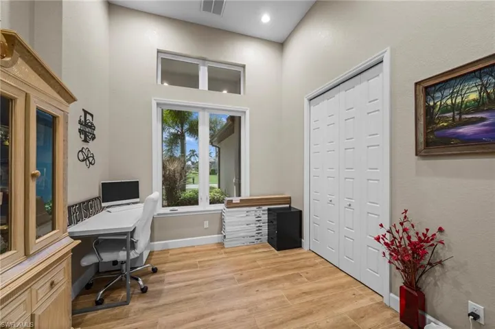 Home office with light wood finished floors, a towering ceiling, and a textured wall