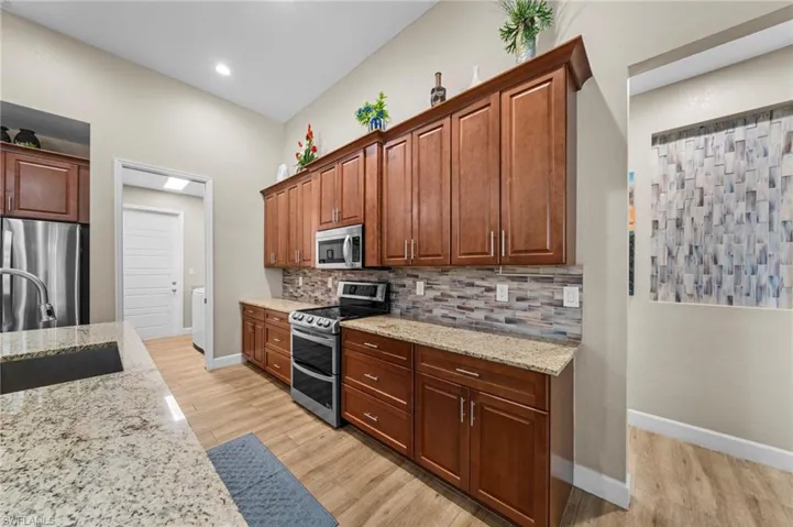 Kitchen featuring stainless steel appliances, decorative backsplash, light wood-type flooring, light stone countertops, and brown cabinets