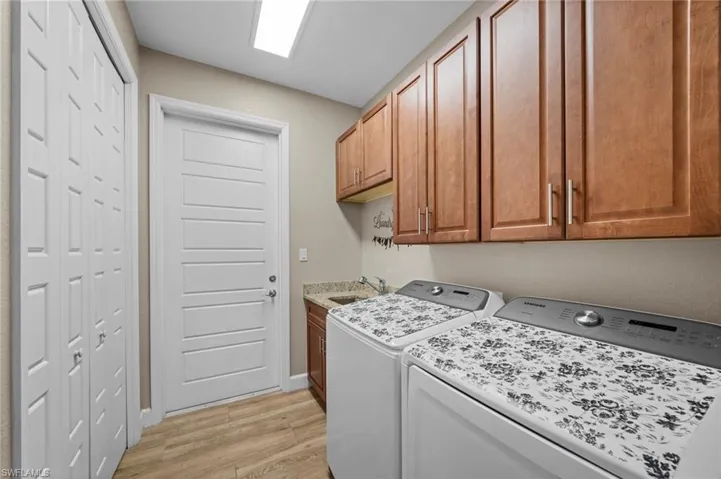 Laundry room featuring washing machine and clothes dryer, cabinet space, and light wood-type flooring