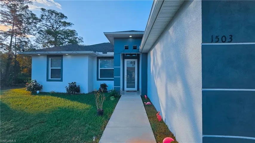 Property entrance featuring a lawn, stucco siding, and a shingled roof