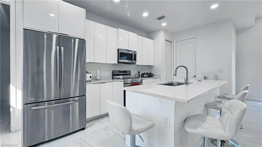 Kitchen featuring stainless steel appliances, a breakfast bar area, white cabinets, modern cabinets, and light marble finish floors
