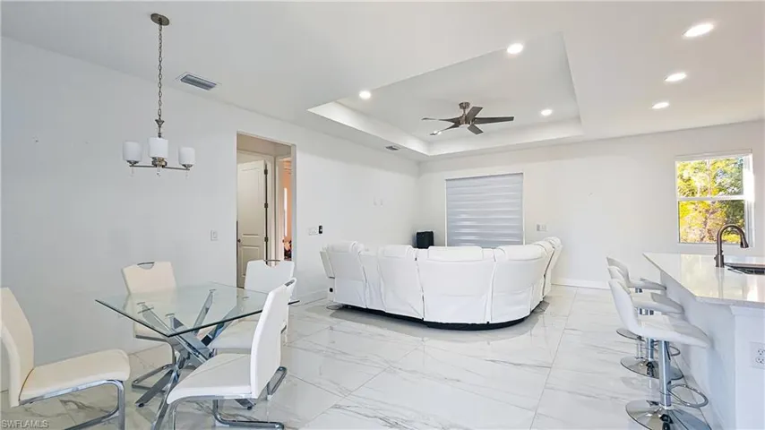 Living area with a tray ceiling, light marble finish flooring, recessed lighting, a chandelier, and a ceiling fan