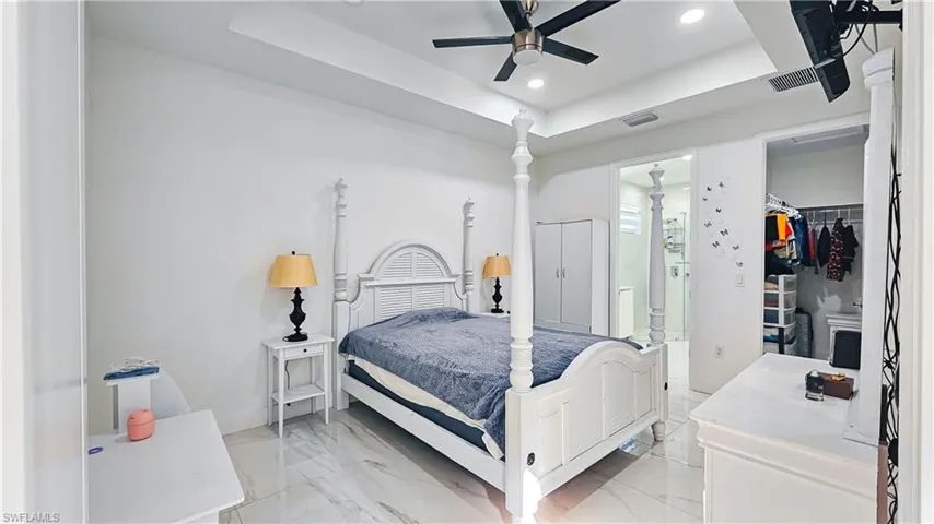 Bedroom featuring a tray ceiling, light marble finish floors, a walk in closet, recessed lighting, and ensuite bathroom