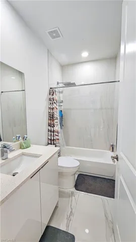 Bathroom with vanity, shower / tub combo, marble finish floors, and recessed lighting