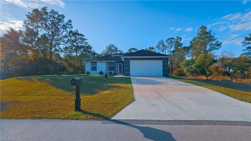 Ranch-style home featuring a front lawn, driveway, a garage, and stucco siding