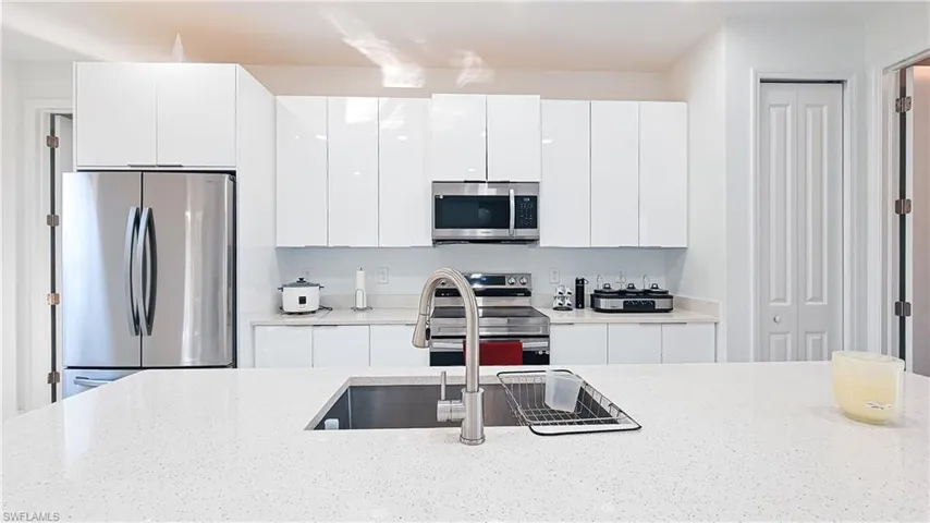 Kitchen with appliances with stainless steel finishes, modern cabinets, white cabinets, and light stone countertops
