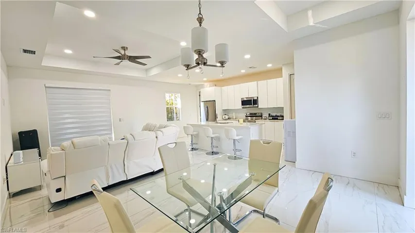 Dining area featuring light marble finish floors, a tray ceiling, recessed lighting, and ceiling fan