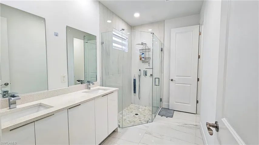 Bathroom with a shower stall, double vanity, marble finish floors, and recessed lighting