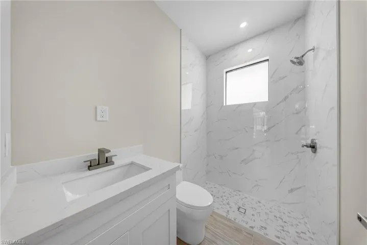 Bathroom featuring a single vanity with an integrated sink and quartz-finish countertop, a walk-in shower with large format tile walls, a mosaic tile shower floor, a ceiling-mounted shower head, and a transom window