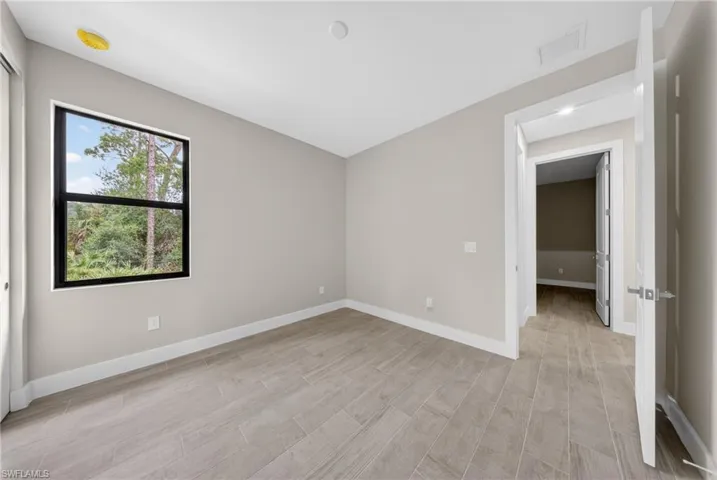 Interior room featuring wood-finish tile flooring, neutral wall tones, a black-framed window with exterior landscaping, a white door with a polished chrome handle, and recessed ceiling lighting