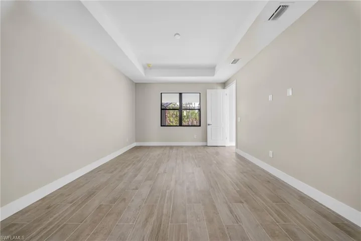 Spacious room featuring wood-finish tile flooring, neutral wall tones, a tray ceiling, and a large window with dark trim