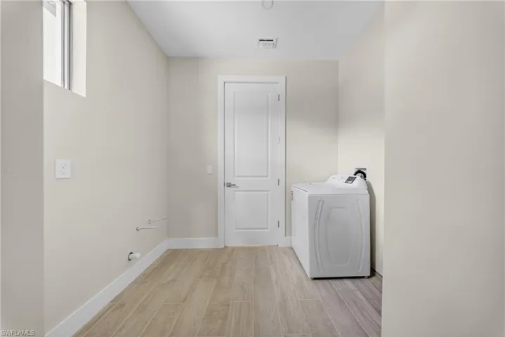 Laundry room featuring wood-finish flooring, a white paneled door, and a high window