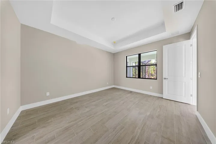 Spacious room featuring a tray ceiling, wood-finish tile flooring, neutral wall tones, modern baseboards, and a contemporary two-panel interior door