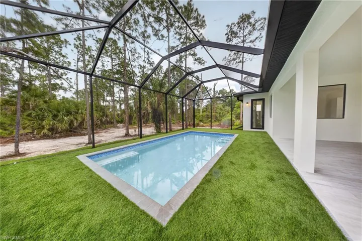 Screened pool enclosure featuring a rectangular swimming pool with integrated steps, artificial turf, and a surrounding paved coping