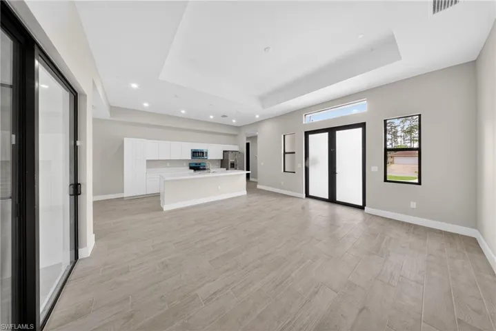 Open-concept living area featuring wood-finish tile flooring, recessed lighting, and a tray ceiling