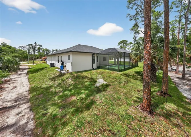 Rear exterior showcasing a screened pool enclosure, lush green lawn, mature trees, and a gravel pathway