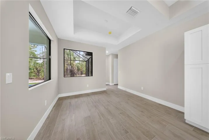 Spacious room featuring wood-finish tile flooring, tray ceilings, and neutral wall tones