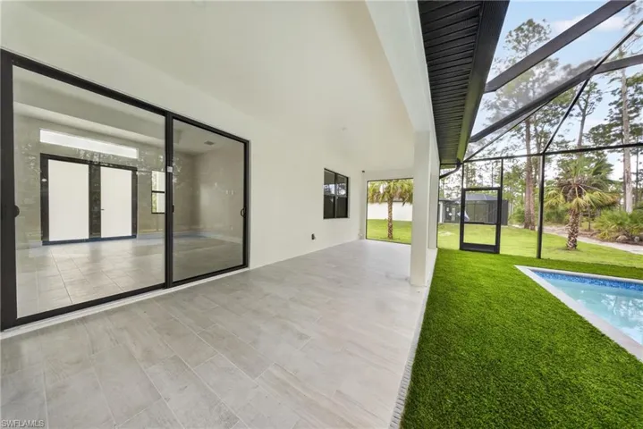 Screened-in outdoor patio featuring a swimming pool, turf grass area, and a covered section with wood-finish tile flooring