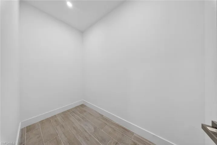 Recessed ceiling light illuminating a neutral-toned room with wood-finish tile flooring and crisp white baseboards