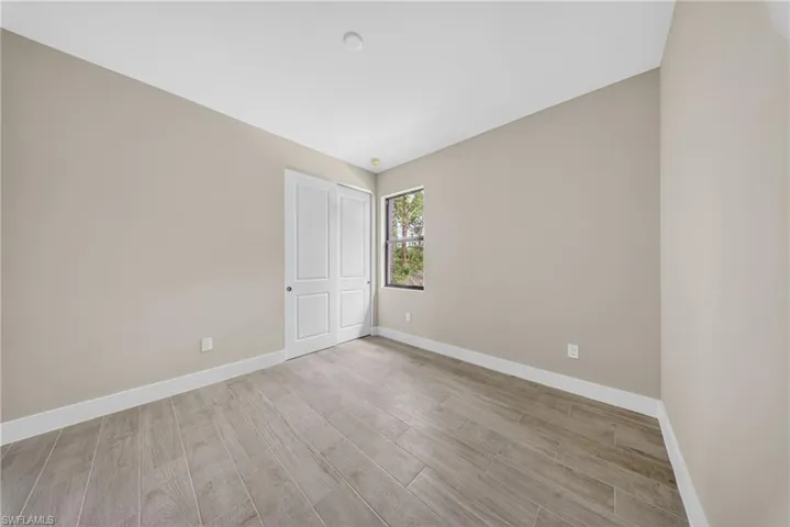 Neutral paint tones complement the wood-finish flooring in this room featuring a window and bi-fold closet doors