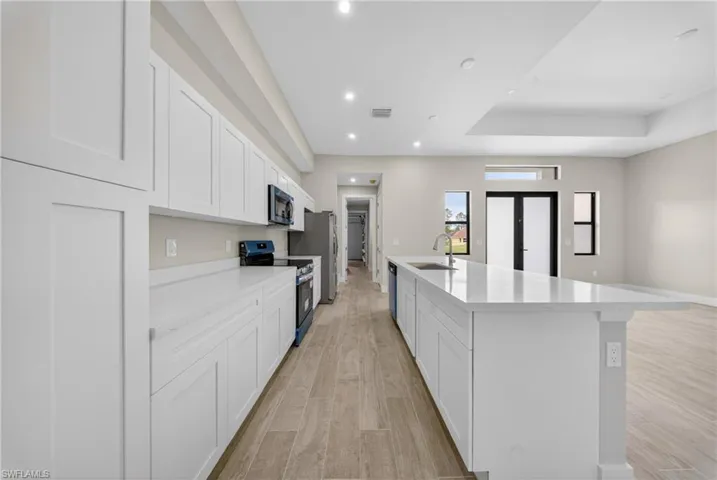 Modern kitchen featuring abundant white cabinetry, light-toned countertops, and wood-finish flooring