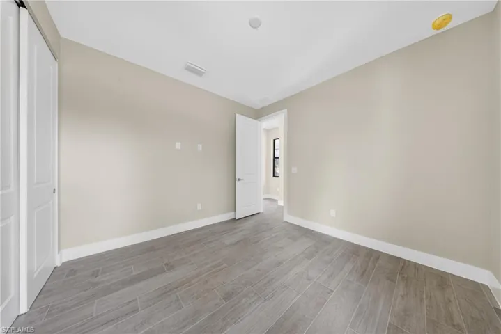 Spacious room featuring wood-finish tile flooring, neutral wall tones, white baseboards, and a white interior door