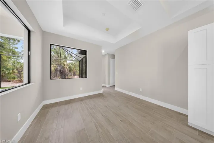 Recessed ceiling with layered trim, light wood-finish flooring, and white baseboards