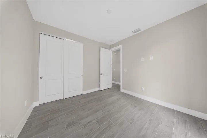 Spacious room featuring light gray wall paint, white baseboards, and wood-finish tile flooring
