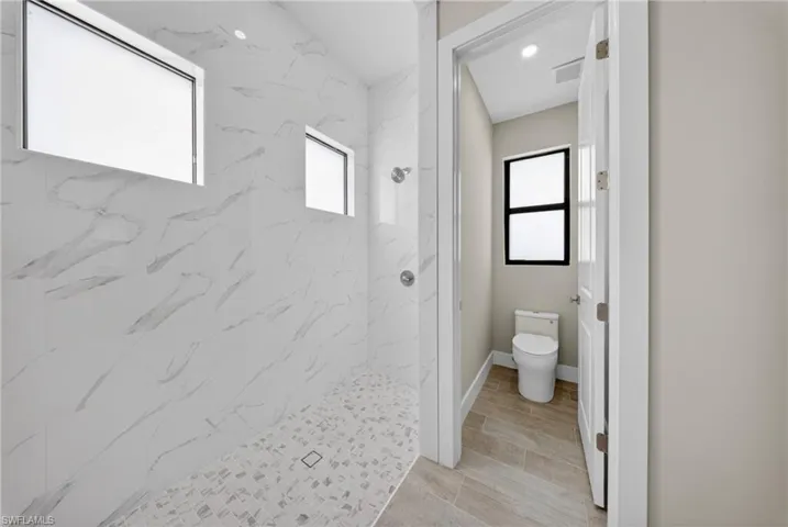 Spacious shower with large format marbled tile walls and mosaic tile flooring