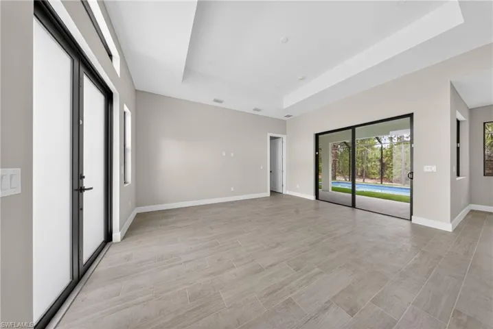 Spacious room featuring tile flooring, a tray ceiling, and dual sliding glass doors opening to a screened pool area
