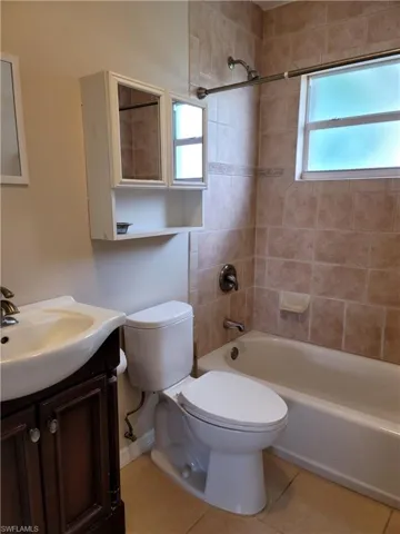 Full bathroom with tiled shower / bath, vanity, toilet, and tile floors