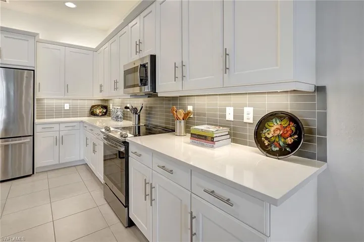 Kitchen featuring decorative backsplash, white cabinets, light tile patterned floors, and appliances with stainless steel finishes
