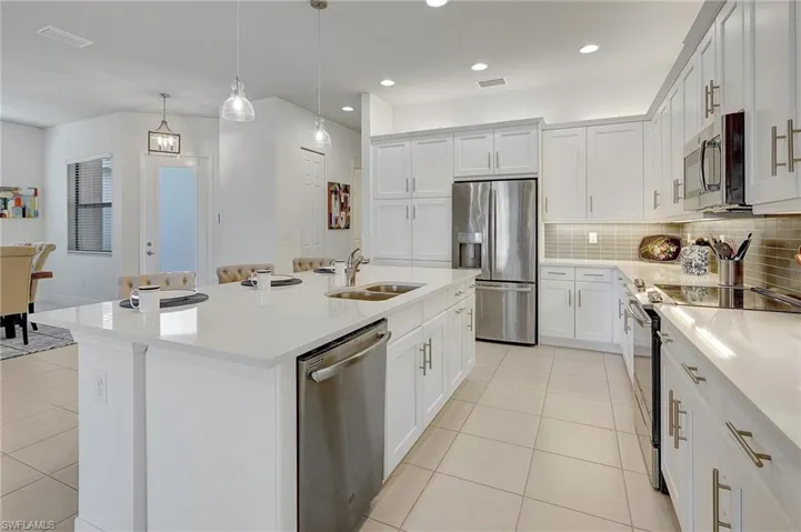 Kitchen featuring appliances with stainless steel finishes, sink, pendant lighting, white cabinetry, and an island with sink