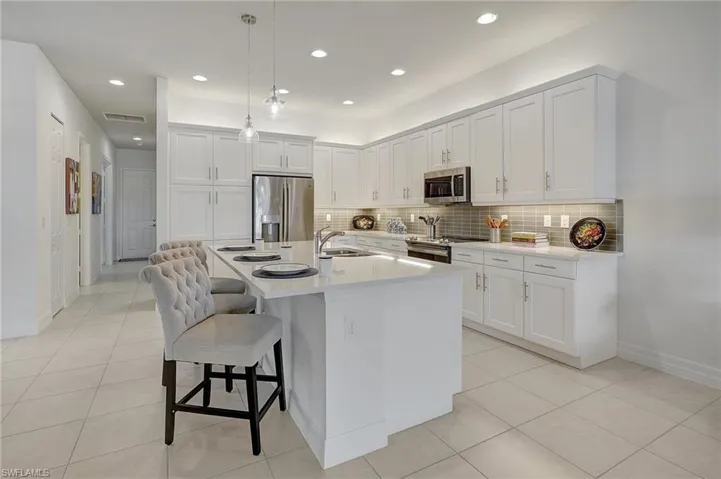 Kitchen with stainless steel appliances, decorative light fixtures, a breakfast bar area, a kitchen island with sink, and white cabinets
