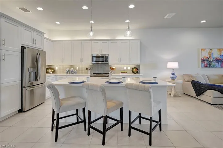 Kitchen featuring a kitchen bar, stainless steel appliances, pendant lighting, white cabinets, and an island with sink