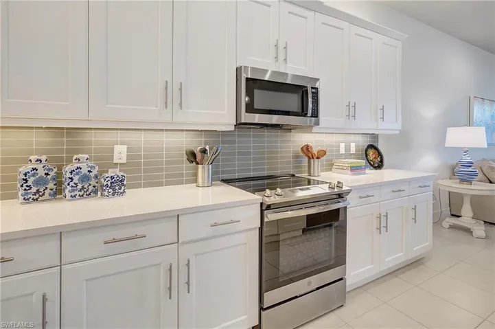 Kitchen with backsplash, light tile patterned flooring, white cabinets, and stainless steel appliances
