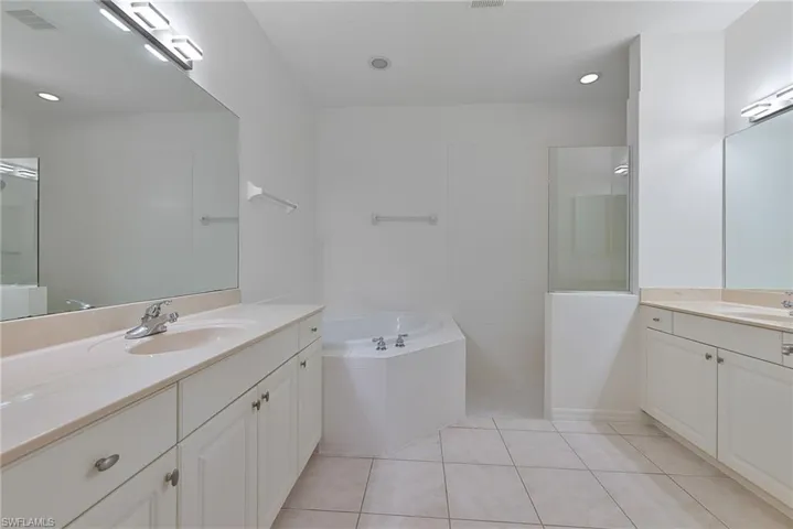 Bathroom featuring a soaking tub, dual separated vanities, and walk in shower