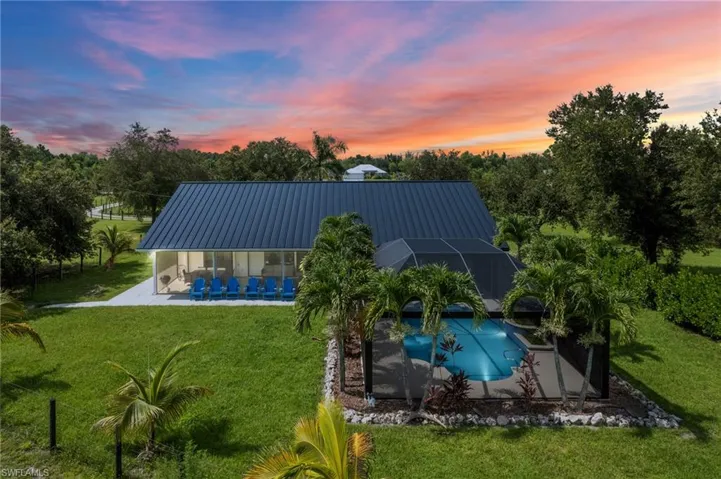 Back of property at dusk featuring an outdoor pool, a patio, a yard, a metal roof, and a lanai