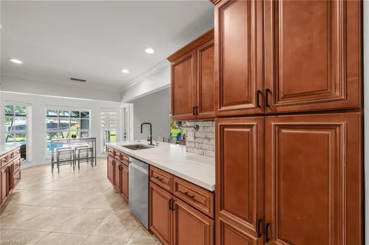 Kitchen with brown cabinets, ornamental molding, light tile patterned floors, light stone counters, and tasteful backsplash