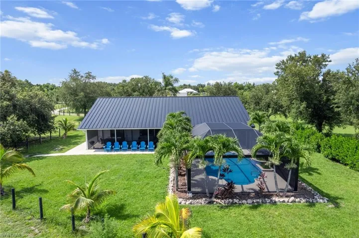 Back of house with a patio, an outdoor pool, a metal roof, a lawn, and a lanai