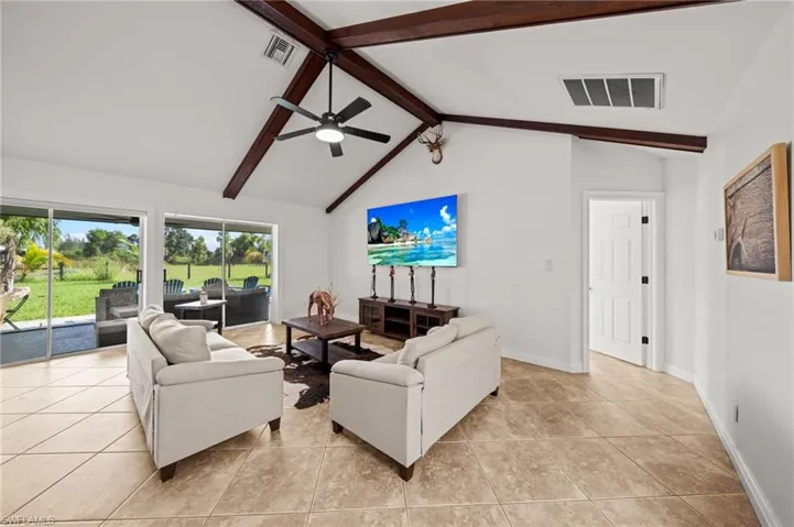 Living room featuring beamed ceiling, light tile patterned floors, a ceiling fan, and high vaulted ceiling