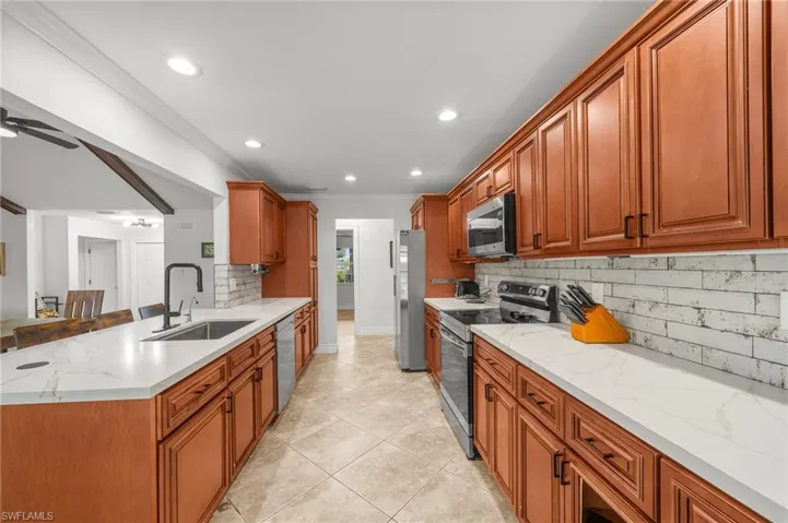 Kitchen with appliances with stainless steel finishes, backsplash, recessed lighting, crown molding, and light tile patterned flooring