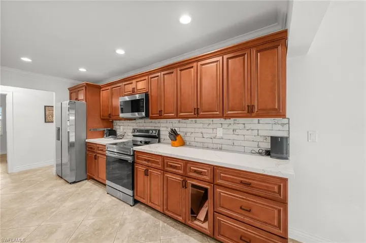 Kitchen with stainless steel appliances, ornamental molding, decorative backsplash, recessed lighting, and light stone counters