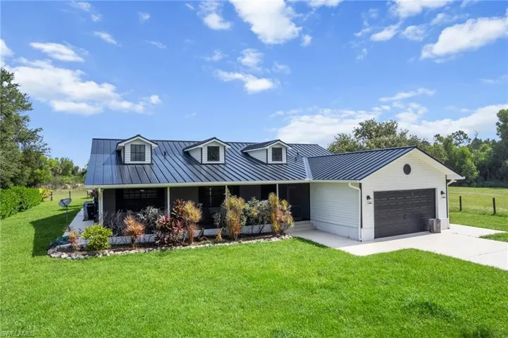 View of front facade featuring a garage, driveway, a front yard, and a metal roof