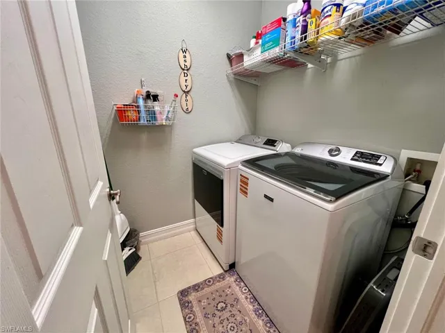 Laundry area with a textured wall, light tile patterned floors, and separate washer and dryer