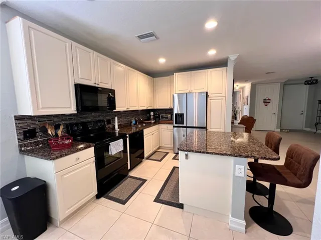 Kitchen featuring dark stone countertops, black appliances, a breakfast bar area, tasteful backsplash, and recessed lighting