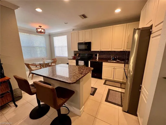 Kitchen featuring dark stone countertops, black appliances, tasteful backsplash, white cabinets, and a center island