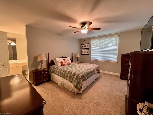 Bedroom with light carpet, ceiling fan, ensuite bathroom, and a textured ceiling